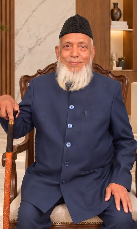 Mr. Abdul Latif Agarwala seated in a navy bandhgala and a black cap, his hand on a carved walking cane