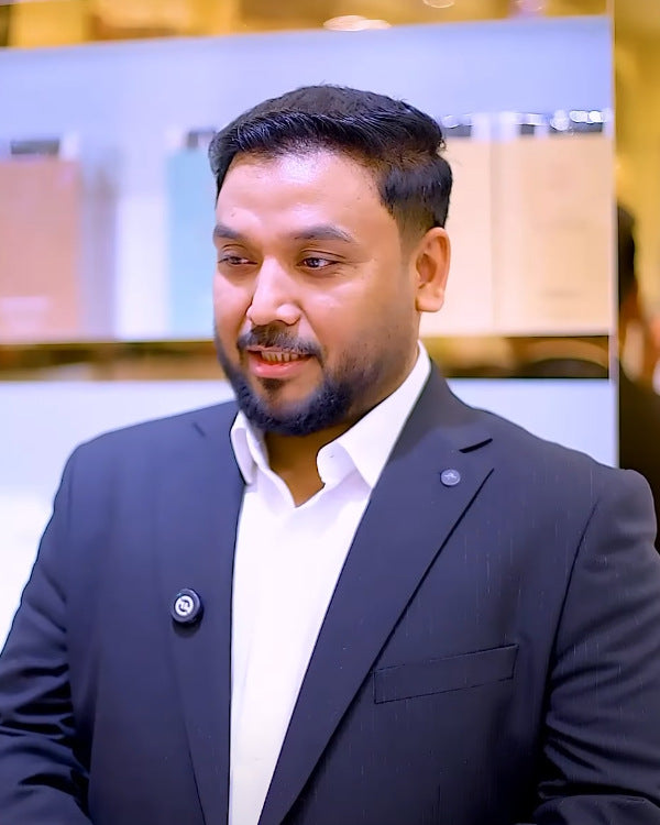Mr. Mohammed Qamar Agarwala in a navy suit and white shirt, in front of perfume shelves