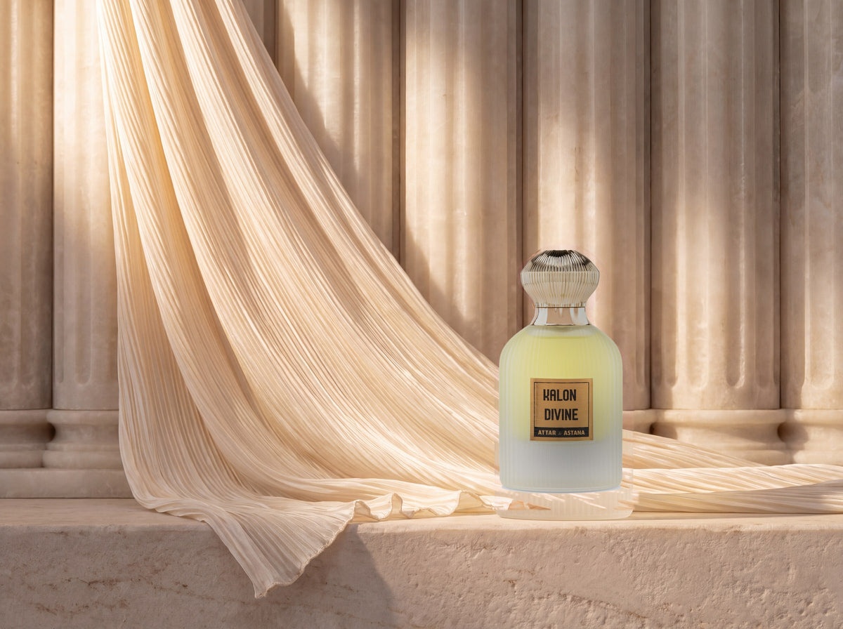 A Kalon Divine bottle on a stone ledge in front of fluted alabaster columns, a fan of pleated cream silk falling across them