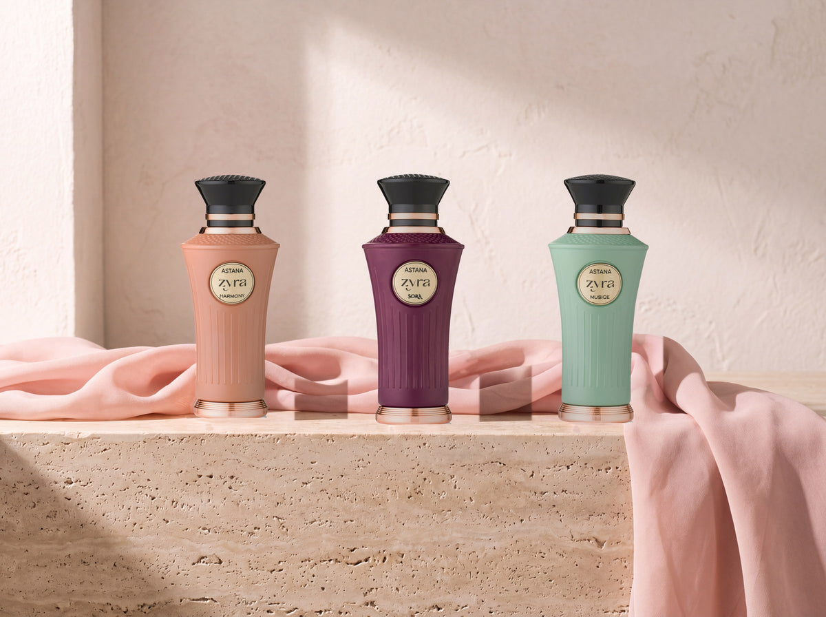 Three Zyra bottles, Harmony, Sora and Musiqe, standing on a travertine ledge in morning window light with blush silk draped beside them